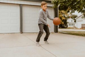 Young boy playing with a basketball in driveway if home
